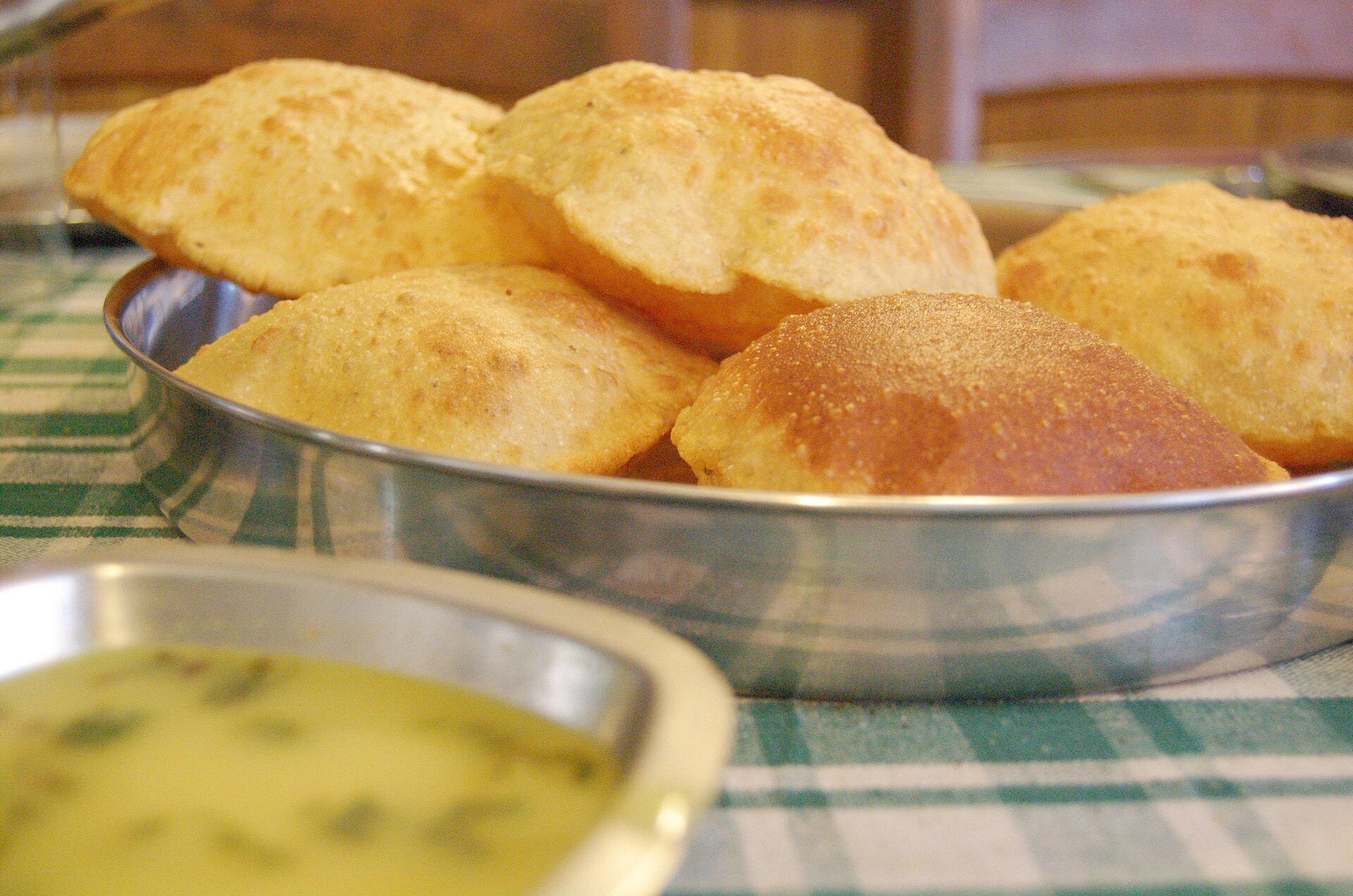 Puffed puris in a steel dish with a bowl of dal alongside