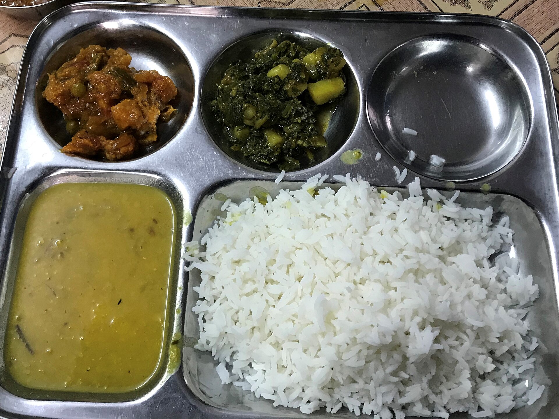 A steel thali of rice, dal, saag and dry sabzi