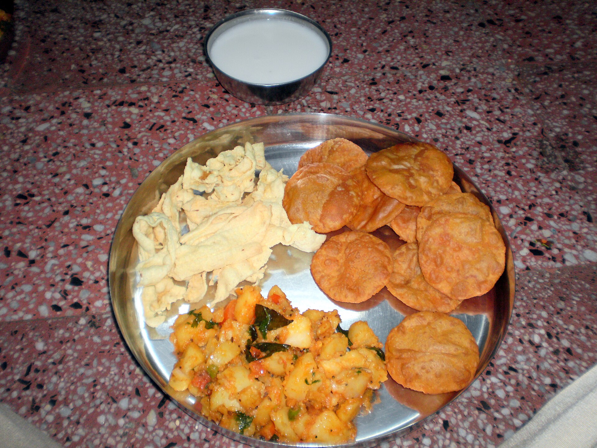 Puri with potato sabzi, papad and a bowl of curd on a steel plate