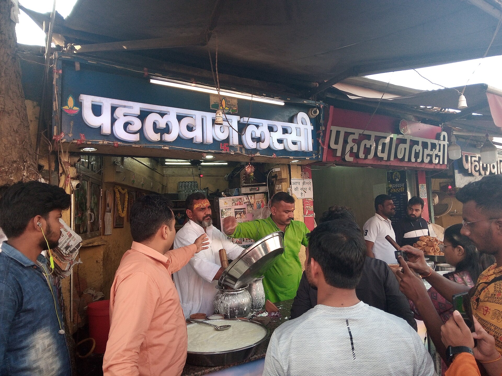 The Pahalwan Lassi counter at Lanka, Varanasi, customers crowding under its Hindi signboard