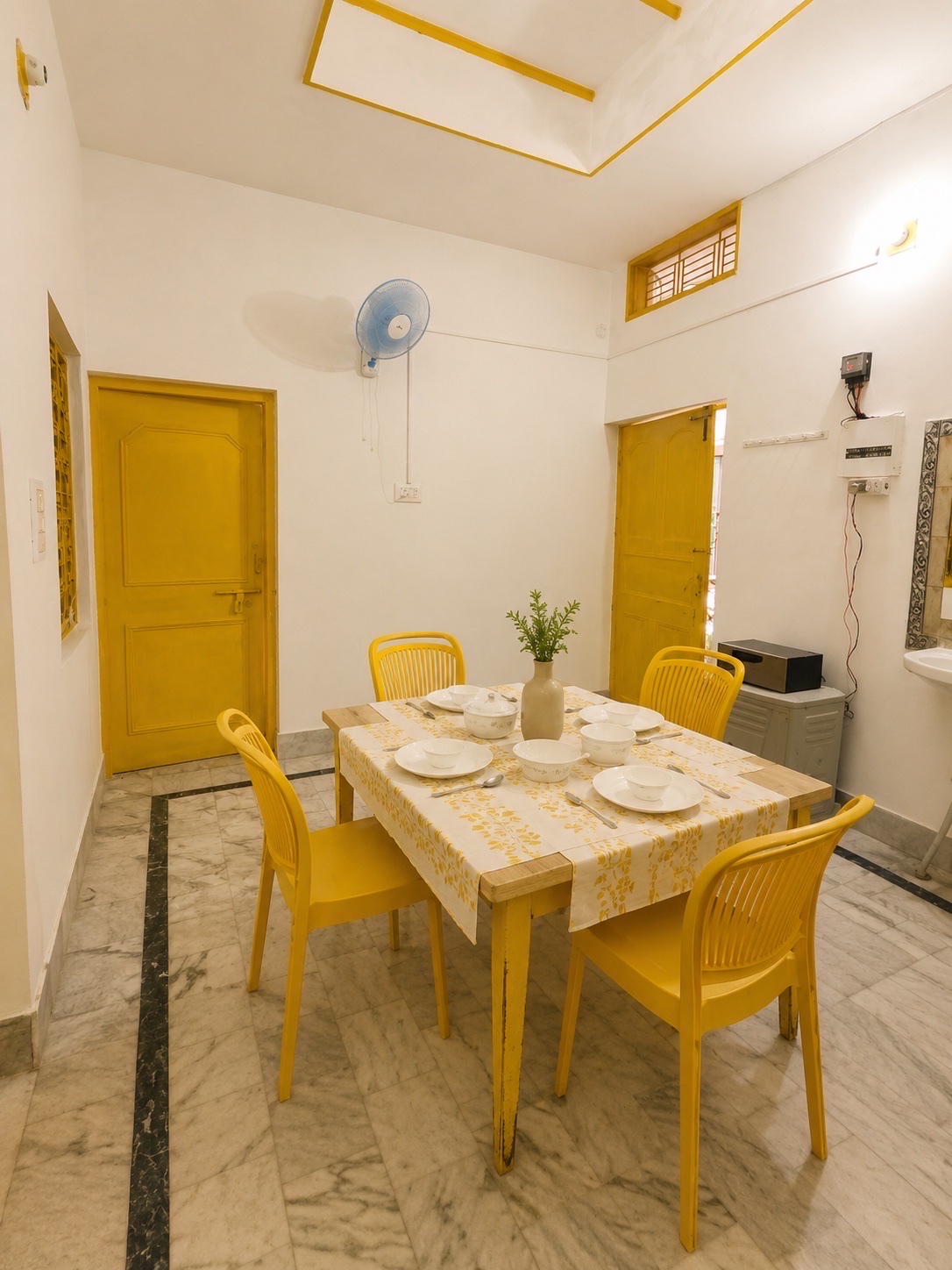 Gardenia, Varanasi: the dining room from the other side, bowls and cutlery set out, a washbasin in the corner and a door open to daylight