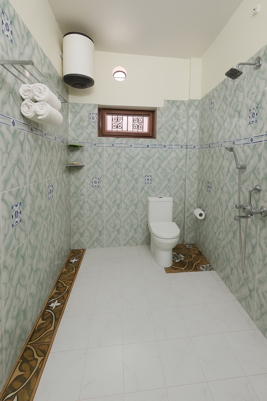 Pratham, Varanasi: bathroom with rolled white towels on a rack, overhead water heater, shower with a hand spray and a western toilet