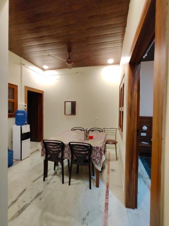Pratham, Varanasi: shared dining room with a checked-cloth table and six chairs, water dispenser in the corner, wooden ceiling above marble flooring
