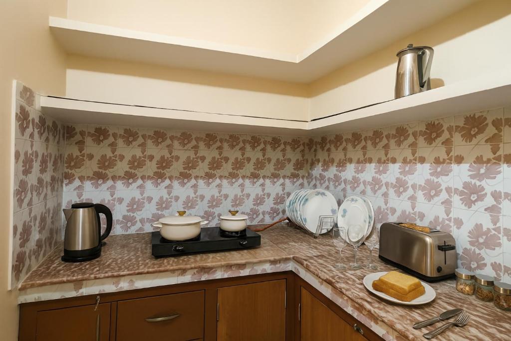 Pratham, Varanasi: corner kitchen counter with a two-burner stove, kettle, toaster and stacked crockery under an open shelf