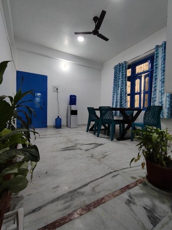 Santorini, Varanasi: open hall with dining table and teal chairs, water dispenser by the blue door and potted plants on the marble floor
